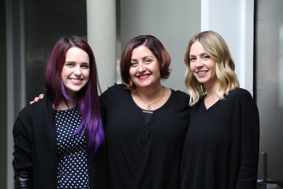 Three women with different hair colors smiling for a portrait while wearing black tops.