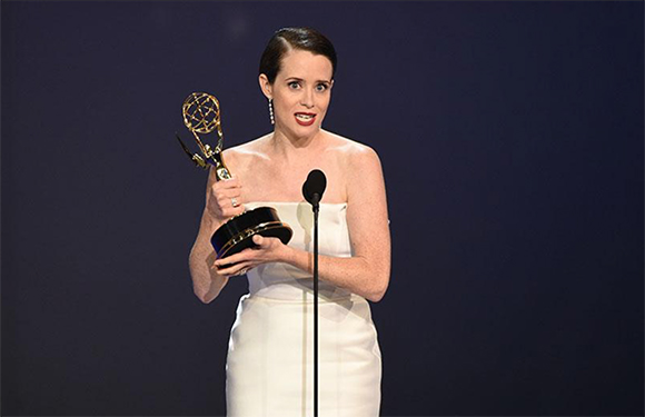 A woman in a white strapless dress holds an Emmy award while standing at a microphone.