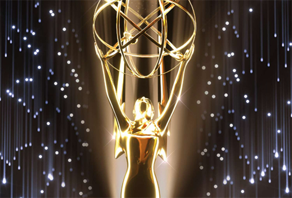 A golden Emmy Award trophy held aloft against a dark, shimmering background of light streaks.