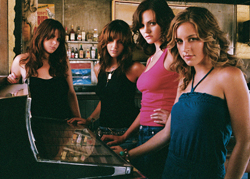 Four young women with long hair posing together in a bar near a jukebox.