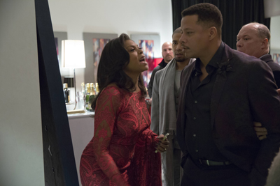 A woman in a red dress looks upward with an intense expression as men stand closely behind her.