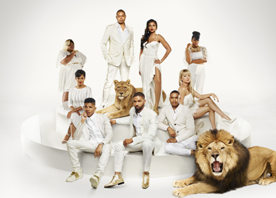 A group of people in white outfits posing with two lions against a white background.
