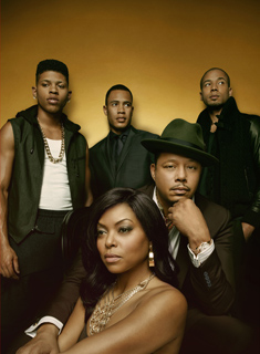 Five people in stylish clothing pose together against a solid gold backdrop.