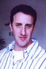A man with dark hair wearing a white shirt with blue vertical stripes.