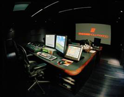 A dark editing studio featuring a large desk with multiple computer monitors and a projection screen.