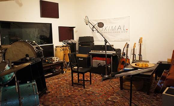 A recording studio with drums, guitars, keyboards, congas, and microphones on a patterned rug.