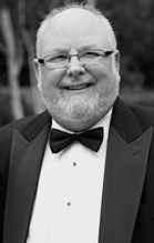 A smiling man with glasses and a beard wearing a tuxedo and bowtie.
