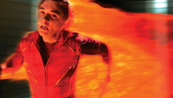 A man in a red superhero suit flying through a trail of orange and yellow flames.