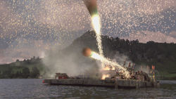 Fireworks and bright sparks erupting from a barge on a lake against a backdrop of hills and a cloudy sky.