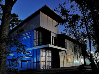 A modern two-story building with blue corrugated panels and grey upper siding under a dark blue twilight sky.