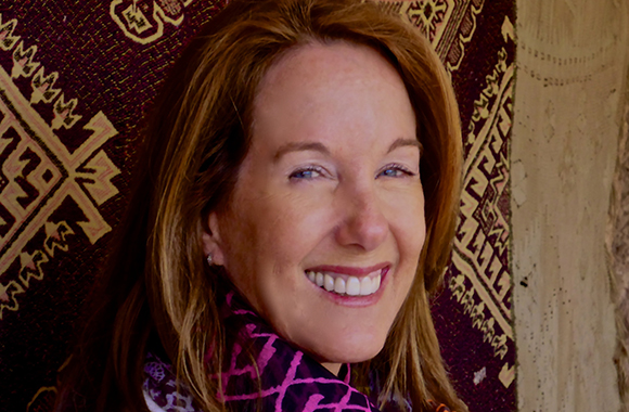 A smiling woman with light brown hair wearing a pink patterned scarf.