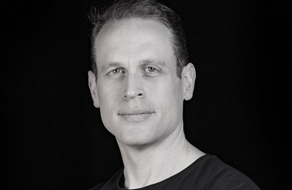 Black and white headshot of a man looking forward against a dark background.
