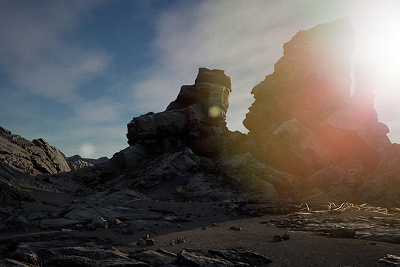 Large, dark rock formations silhouetted against a bright, sunlit sky in a desolate landscape.