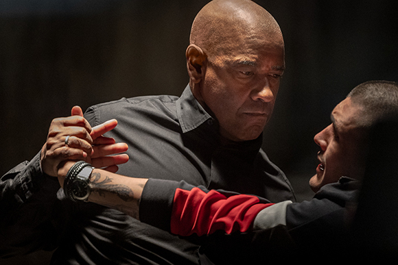 A bald man in a black shirt grips the arm of a younger man in a red and black shirt.