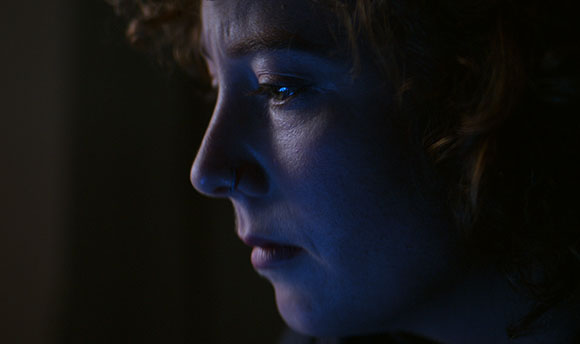 A close-up profile of a person's face lit by a cool blue light against a dark background.