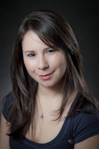 A woman with long dark hair and a dark blue shirt smiles slightly against a dark background.