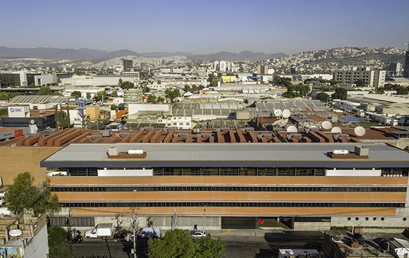 Aerial view of a large industrial building in a dense city with hills in the background.