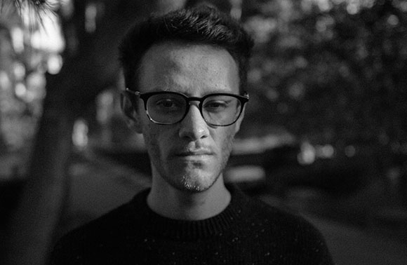 Black and white close-up portrait of a man with glasses looking directly at the camera.