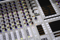 A close-up, angled view of a professional audio mixing console with many illuminated knobs and sliders.