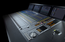 A large digital audio mixing console with numerous sliders, knobs, and four integrated display screens.