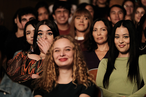 A diverse group of people sitting in rows, looking toward the front with various facial expressions.