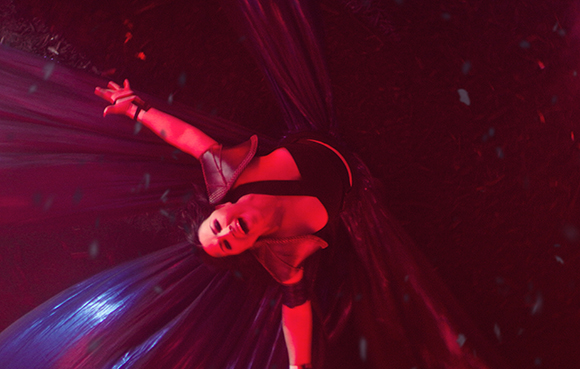 A person lying amidst flowing, translucent red fabric under intense red lighting.