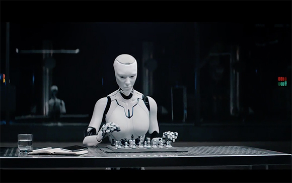 A white humanoid robot sits at a table, focused on a game of chess in a dark room.