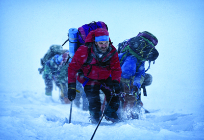 A group of hikers in heavy gear struggle through a heavy snowstorm on a snowy slope.
