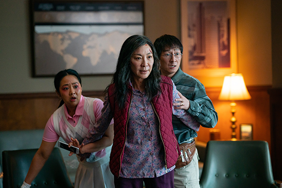 Three people with worried expressions stand in a room near a lamp and a world map.