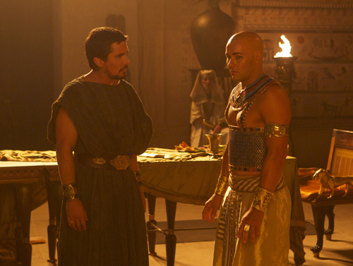 Two men in ancient Egyptian attire stand in a room with a table and a torch.