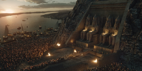 Giant stone statues carved into a cliff overlooking a crowded harbor at sunset.