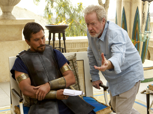 A director in a blue shirt gestures toward an actor wearing dark leather armor sitting in a chair.