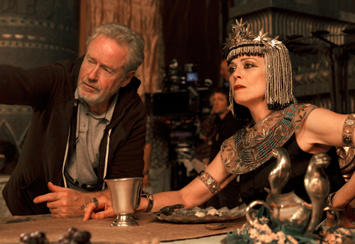 A man in a dark jacket leans toward a woman wearing an ornate Egyptian headdress and jewelry.