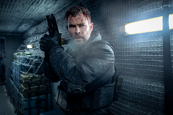 A man with facial blood stains aims a handgun while wearing dark tactical clothing.