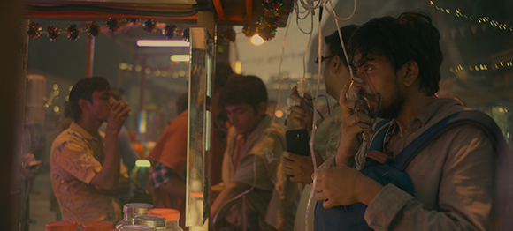 Several young men stand around an outdoor food stall at night, drinking from small cups.