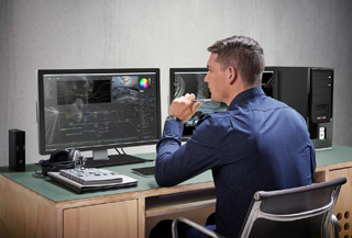 A man in a blue shirt sits at a desk looking at two computer monitors displaying technical data.