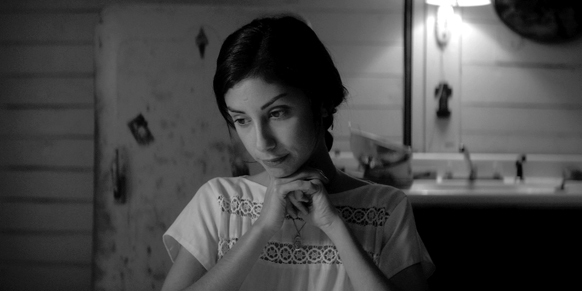 Black and white portrait of a woman looking downward with her hands clasped under her chin.