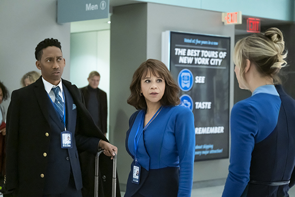 A man in a uniform and a woman in a blue blazer look toward a blonde woman in a blue uniform.