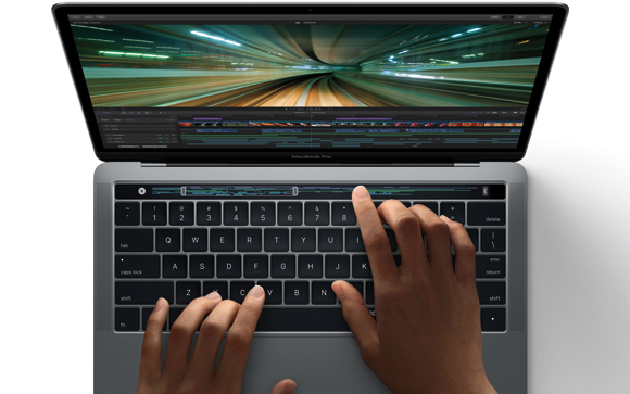 Hands typing on the keyboard of a MacBook Pro displaying video editing software.