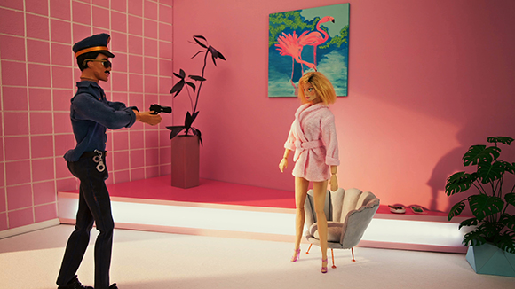 A male doll in a blue uniform points a toy gun at a blonde female doll wearing a pink robe.