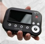 A person holds a small, black handheld electronic device with a screen and various buttons.