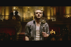 A man in a grey shirt holds a decorative metal device in a dimly lit, ornate ballroom.