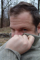 A man pulls a grey sweater collar up to cover his nose while looking forward.