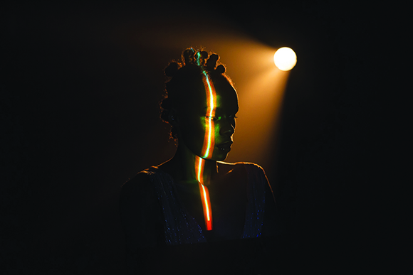 A person silhouetted in darkness with vertical stripes of yellow, green, and red light across their face and chest.