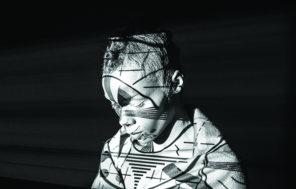 Black and white portrait of a person with geometric light and shadow patterns across their face and clothing.