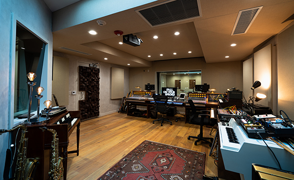 A professional music recording studio featuring a large mixing console, synthesizers, and wooden floors.