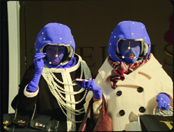 Two people in blue hoods and gloves holding handbags and a phone.