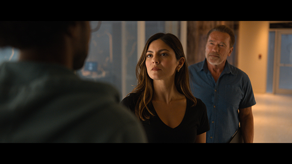 A woman with long dark hair and a man in a blue shirt look toward a person in the foreground.