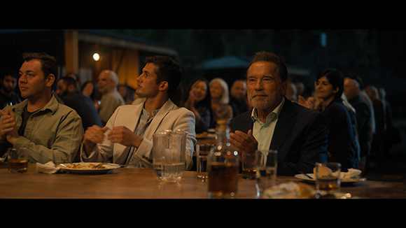 Several people sit around a wooden table in a dimly lit room, engaged in conversation.