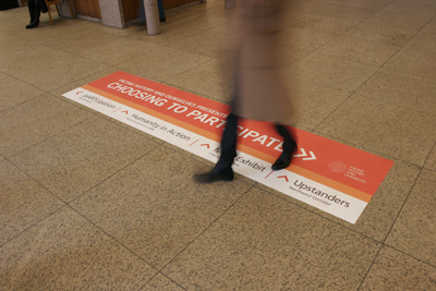A red rectangular floor decal with white text reading 'CHOOSING TO PARTICIPATE' on a tiled floor.